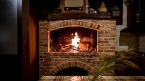 Une cheminée en briques avec un feu, une radio placée au-dessus, et une table recouverte d’une nappe à carreaux devant.