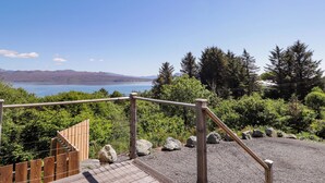 A wooden deck with a metal railing overlooking a lake, surrounded by trees and rocks. - The Lookout (Sleat)