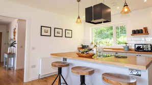 A modern kitchen with a large island, pendant lights, and framed pictures on the wall. - The Lookout (Sleat)