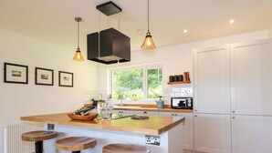 A modern kitchen with a central island, bar stools, pendant lighting, and a view of greenery outside. - The Lookout (Sleat)