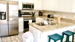 A kitchen with white cabinets, stainless steel appliances, a granite countertop, and two bar stools.