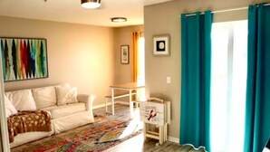 A living room with a white sofa, a colorful rug, a ceiling fan, and a sign that reads "Lobsters Live."