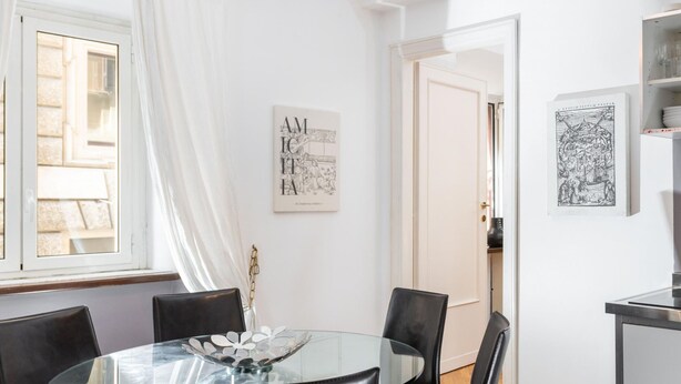 A dining area with a glass table, black chairs, and a white wall with framed artwork. - Corso Vittorio - Campo de Fiori (Rome)