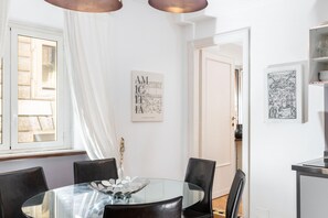 Ein Essbereich mit einem Glastisch, schwarzen Stühlen und einer weißen Wand mit gerahmten Kunstwerken.