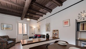 A cozy living room with a sofa, a coffee table, and a dining table with plates and bowls. There are framed pictures on the walls and a clock above the dining table. - Cedro House in Trastevere (Rome)