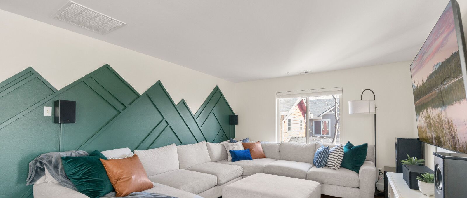 A modern living room with a sectional sofa, a large window, and a painting on the wall.