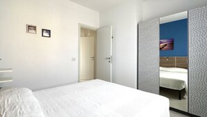 Un dormitori amb un llit, un armari amb mirall i una porta que dóna a una altra habitació.