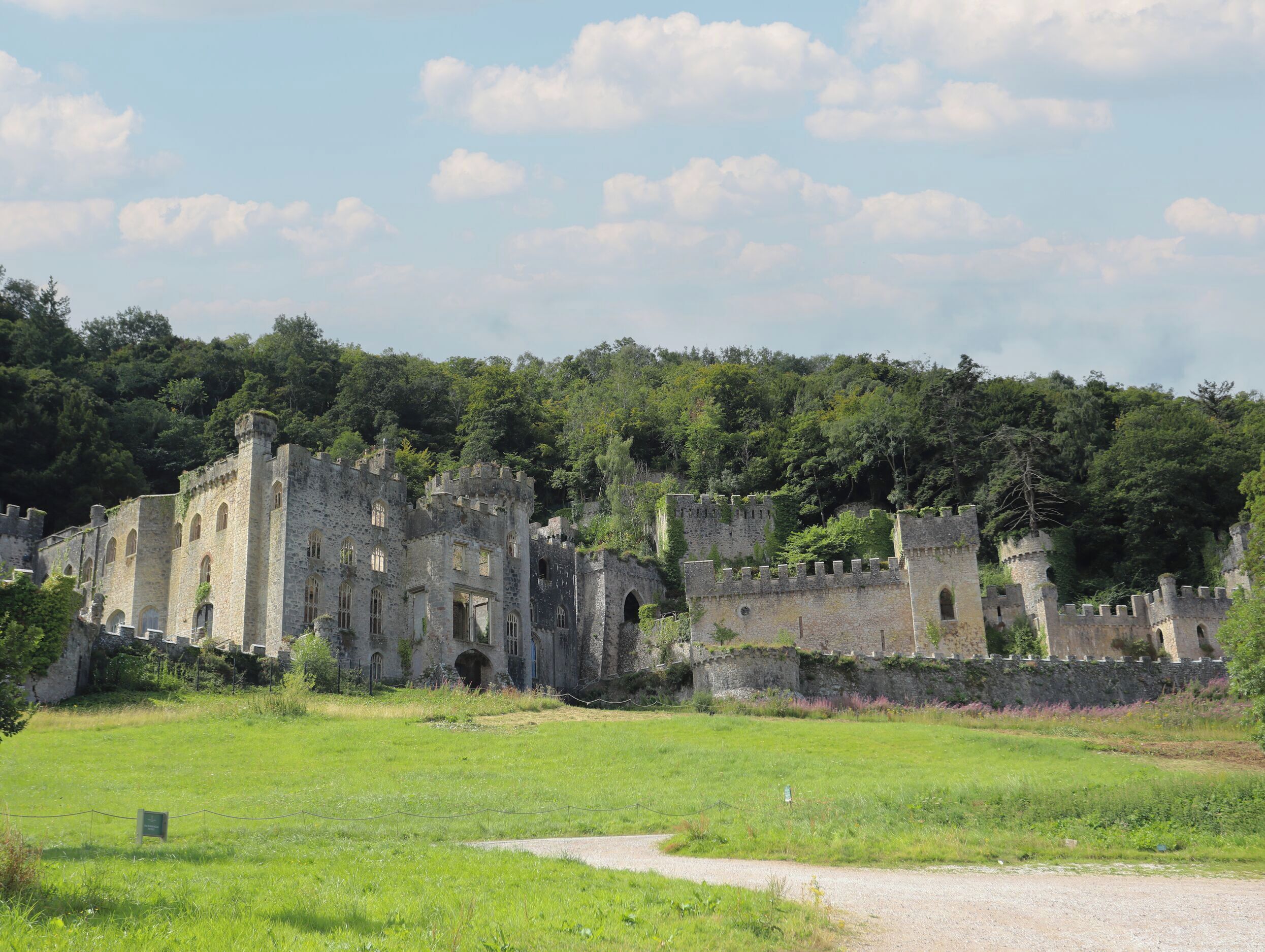 An ancient stone castle with multiple towers and arched windows, surrounded by lush greenery and a clear sky.