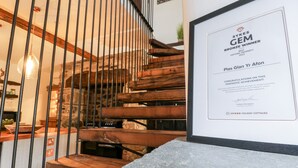 A staircase with wooden steps and metal railings, leading to a room with a stone wall and a framed award certificate on the wall.