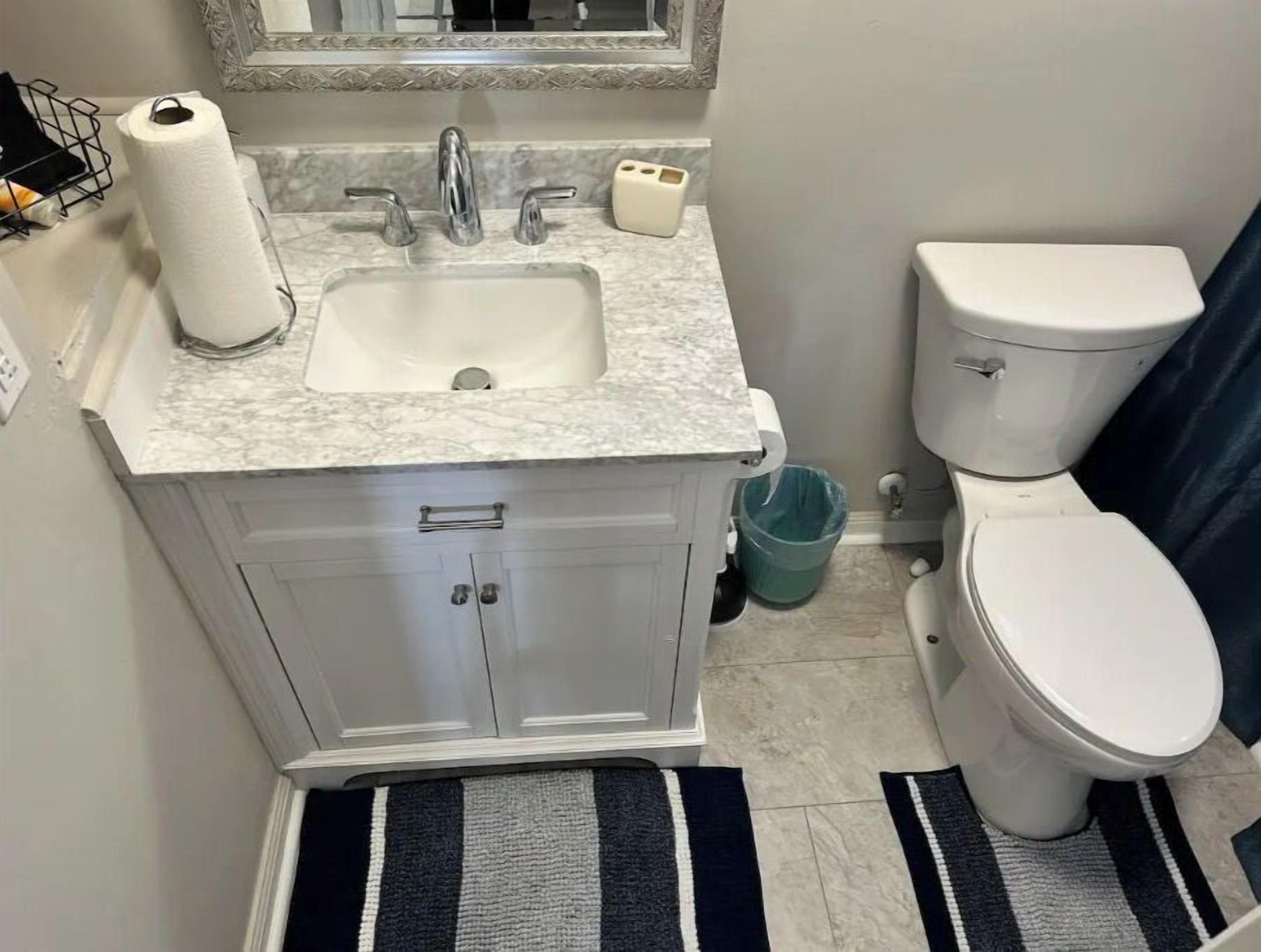 A bathroom with a marble sink, two faucets, a toilet, and a trash can.