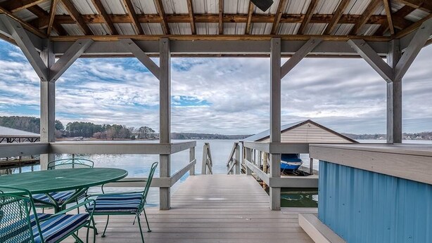 Une terrasse couverte avec vue sur un lac, des rampes en bois et une table avec des chaises.