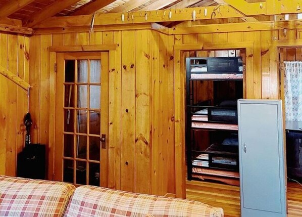 Une pièce de chalet en bois avec un canapé à carreaux, un petit meuble et une fenêtre avec des rideaux.
