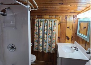 Une salle de bain aux murs lambrissés, équipée d’une douche, de toilettes et d’un lavabo.
