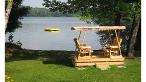 A wooden bench with a table, situated on a grassy area near a lake. - Wendell Cottage (Belgrade)