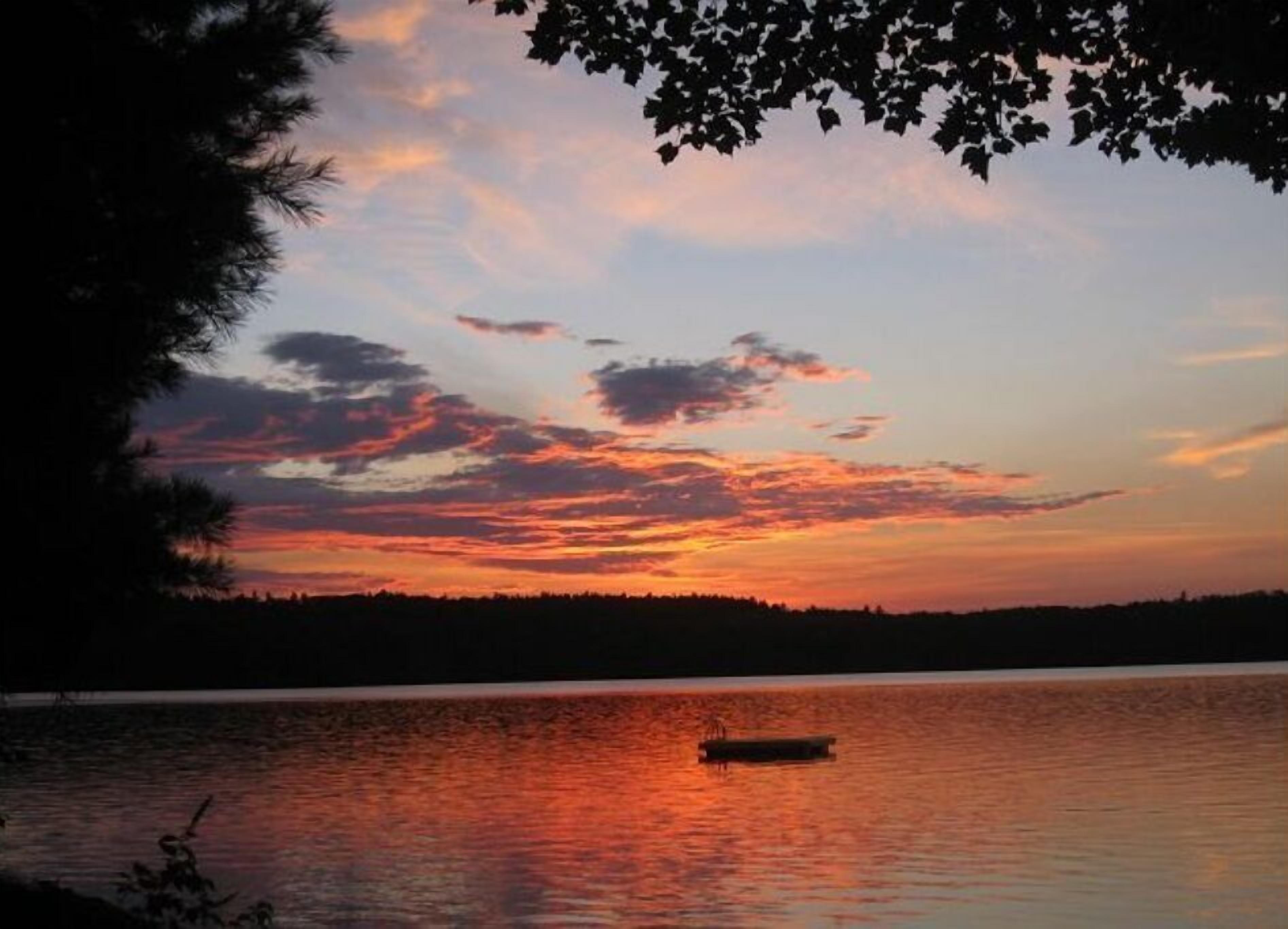 Un tramonto sul lago calmo con una piccola barca al centro.