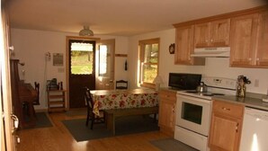 A kitchen with wooden cabinets, a microwave, stove, and a dining area with a table and chairs. - Wendell Cottage (Belgrade)