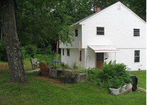 A white two-story house with a front porch, surrounded by a grassy yard and trees.
