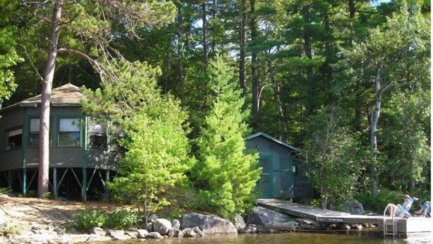 A lakeside cabin with a dock extending into the water, surrounded by dense forest. - Haskell's Lodge on Long Pond! (Belgrade)