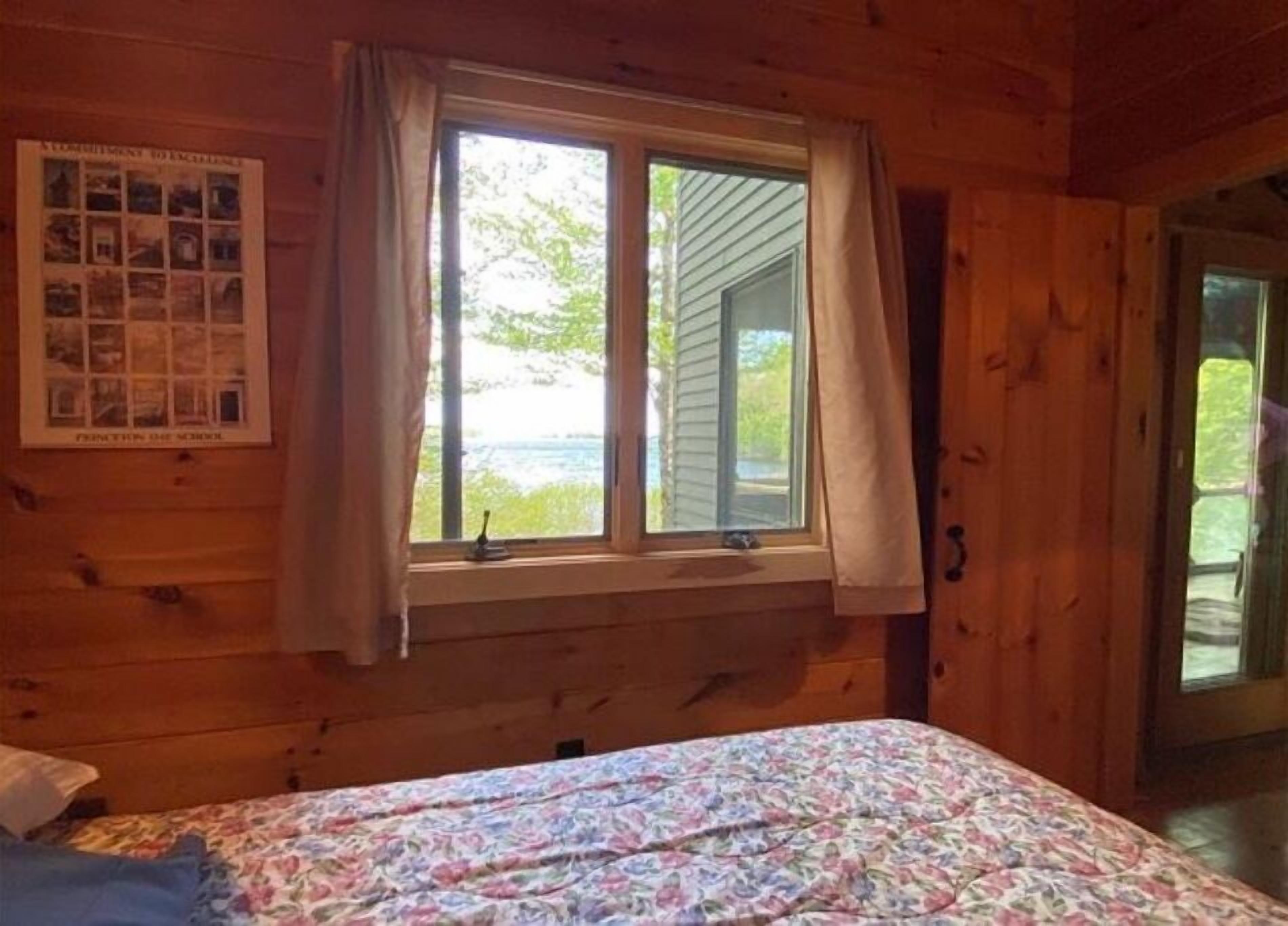 A wooden cabin room with a bed, a window with curtains, and a poster on the wall.