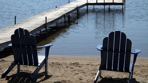 Two Adirondack chairs on a sandy beach with a wooden dock extending into a calm body of water. - Sandy Beach Cottage! (Belgrade)