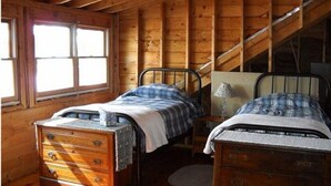 A rustic cabin bedroom with two wooden beds, a dresser, and a window. - Sandy Beach Cottage! (Belgrade)
