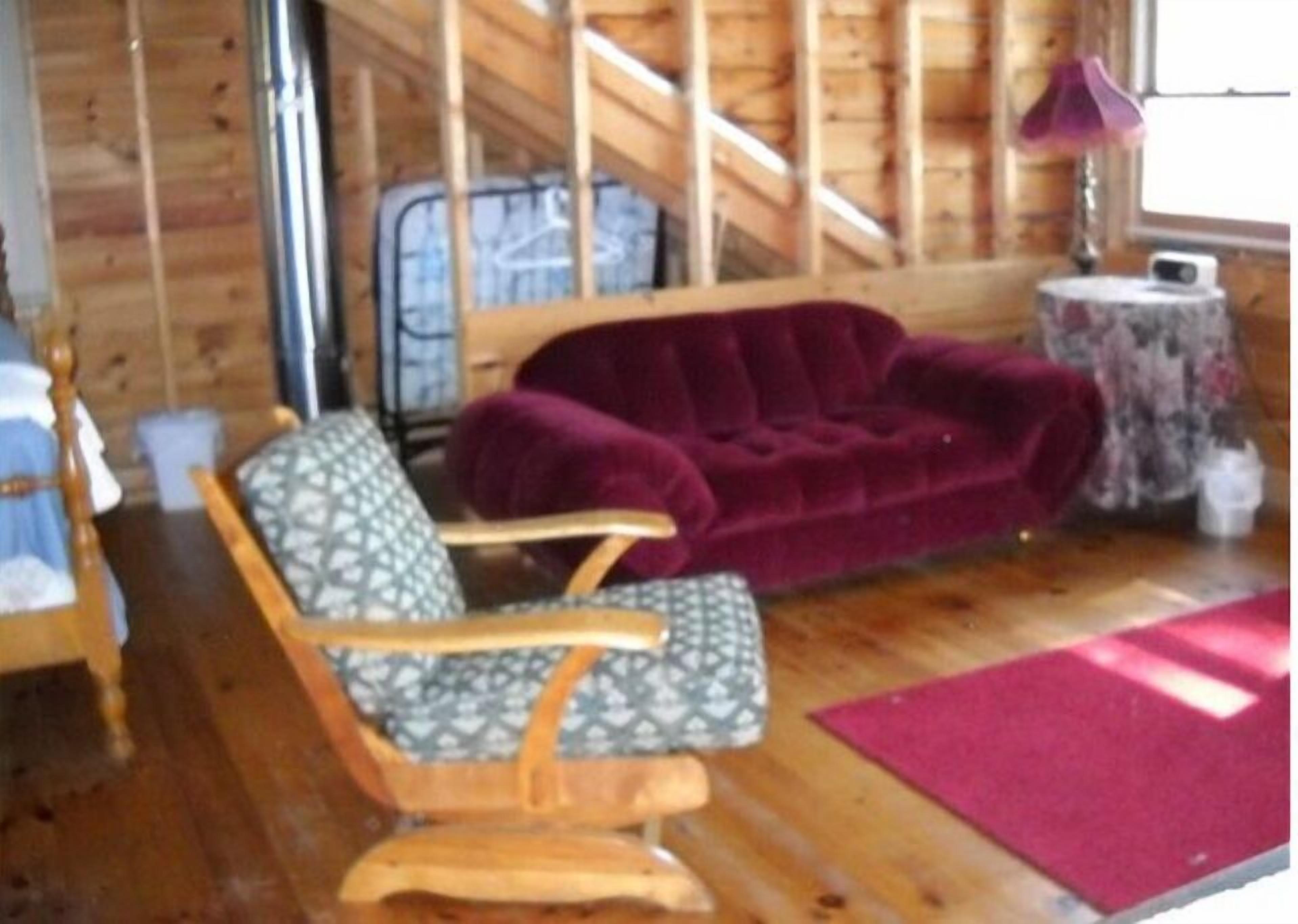 A wooden interior with a wooden rocking chair, a purple sofa, and a small round table with a lamp.