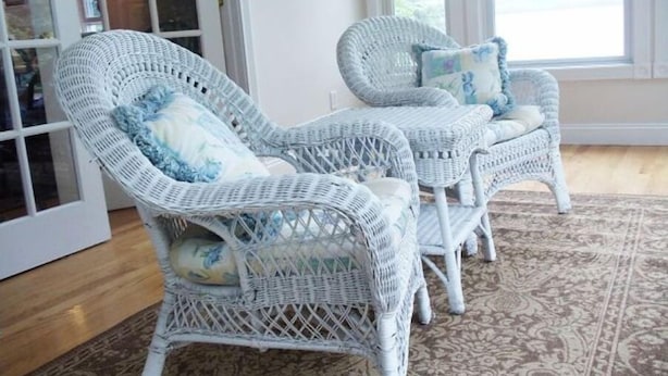 Une pièce meublée avec des meubles en osier, notamment deux chaises et une table, et un tapis à motifs sur le sol.
