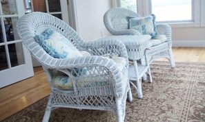 Una habitación con muebles de mimbre, incluyendo dos sillones y una mesa, y un tapiz estampado en el suelo.