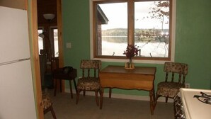 A dining area with a table and four chairs, a window with a view of a lake, and a refrigerator. - Gramp's Camp (Belgrade)