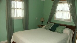 A bedroom with a bed, a nightstand, a lamp, and two windows with curtains. - Gramp's Camp (Belgrade)