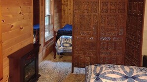 A wooden cabin room with a bed, a fireplace, and a large wooden door with intricate carvings. - Mystic Bungalow (Belgrade)