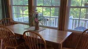 A dining area with a wooden table and chairs, a vase with flowers, and a view of greenery through large windows. - Hidden Cove Camp (Oakland)