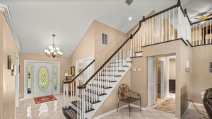 A spacious foyer with a grand staircase, a chandelier, and a red rug leading to a door with stained glass. - Peaceful Private Ranch  Fire Pit  Near WEC, HITS, Rainbow Springs & Devil’s Den (Morriston)