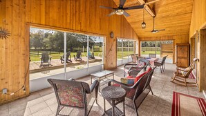 A covered patio area with wicker furniture, large windows, and a ceiling fan. - Peaceful Private Ranch  Fire Pit  Near WEC, HITS, Rainbow Springs & Devil’s Den (Morriston)