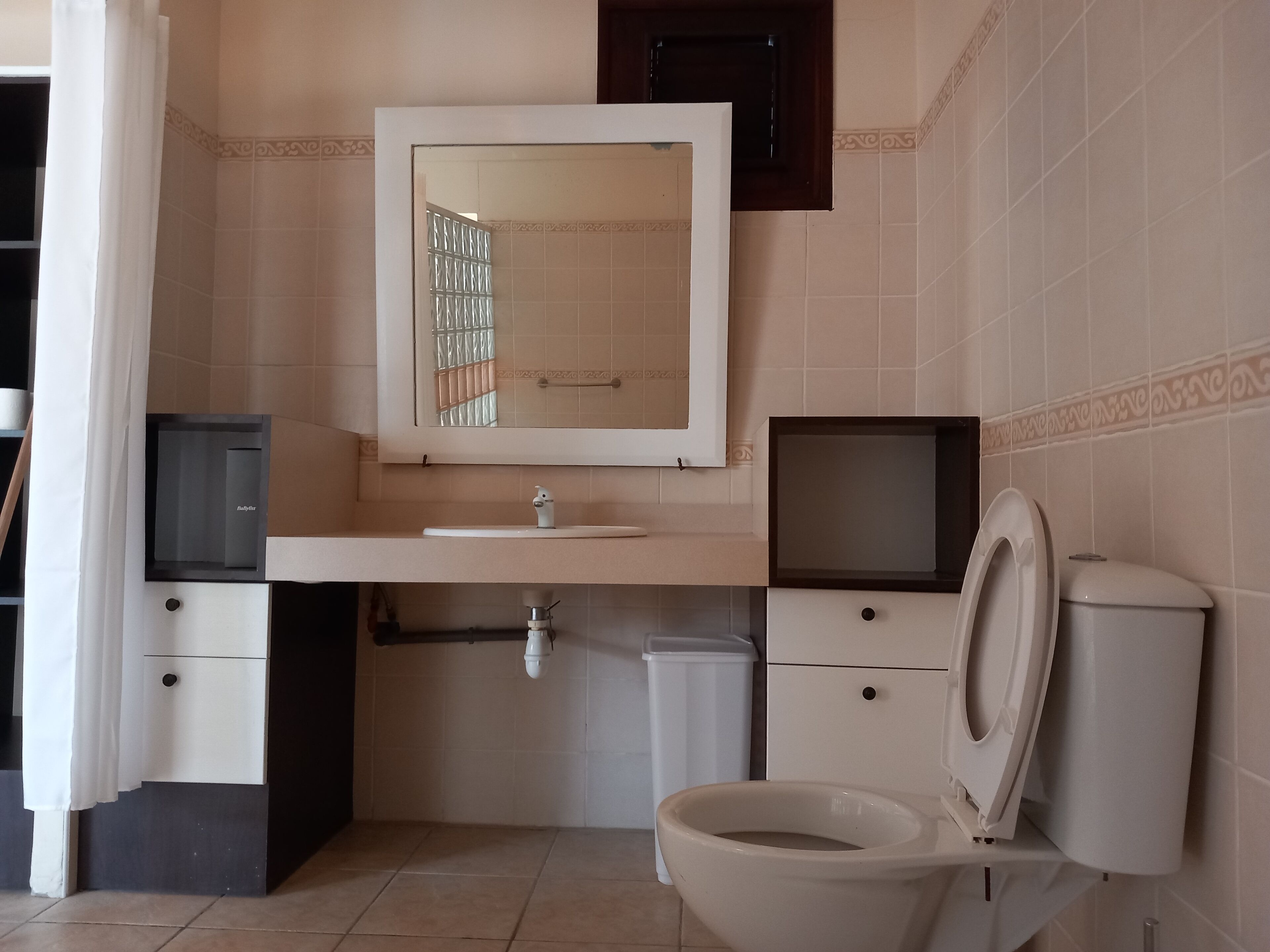 Ein Badezimmer mit Toilette, Waschbecken, Spiegel und Duschbereich.