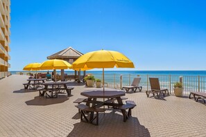 Une terrasse extérieure dotée d’un sol carrelé à motifs hexagonaux, de parasols jaunes, de tables en bois et de chaises longues.