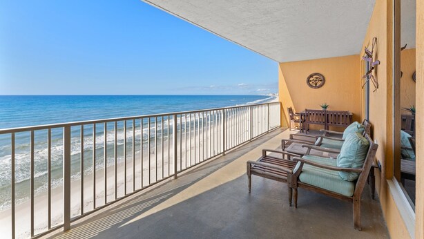 A balcony with a view of the beach and ocean, wooden furniture, and a wall with a decorative plate. - Gulf-front condo w/ pool, hot tub and beach access (Panama City Beach)