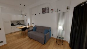 Een knus verblijf met een kitchenette, een bank met kussens, een eethoek en een lamp.