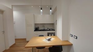 Een kleine keuken met witte kasten, een zwart aanrecht en een houten eettafel met twee stoelen.