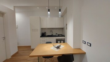 Una cocina compacta con armarios blancos, encimera negra y una mesa de madera con dos sillas.