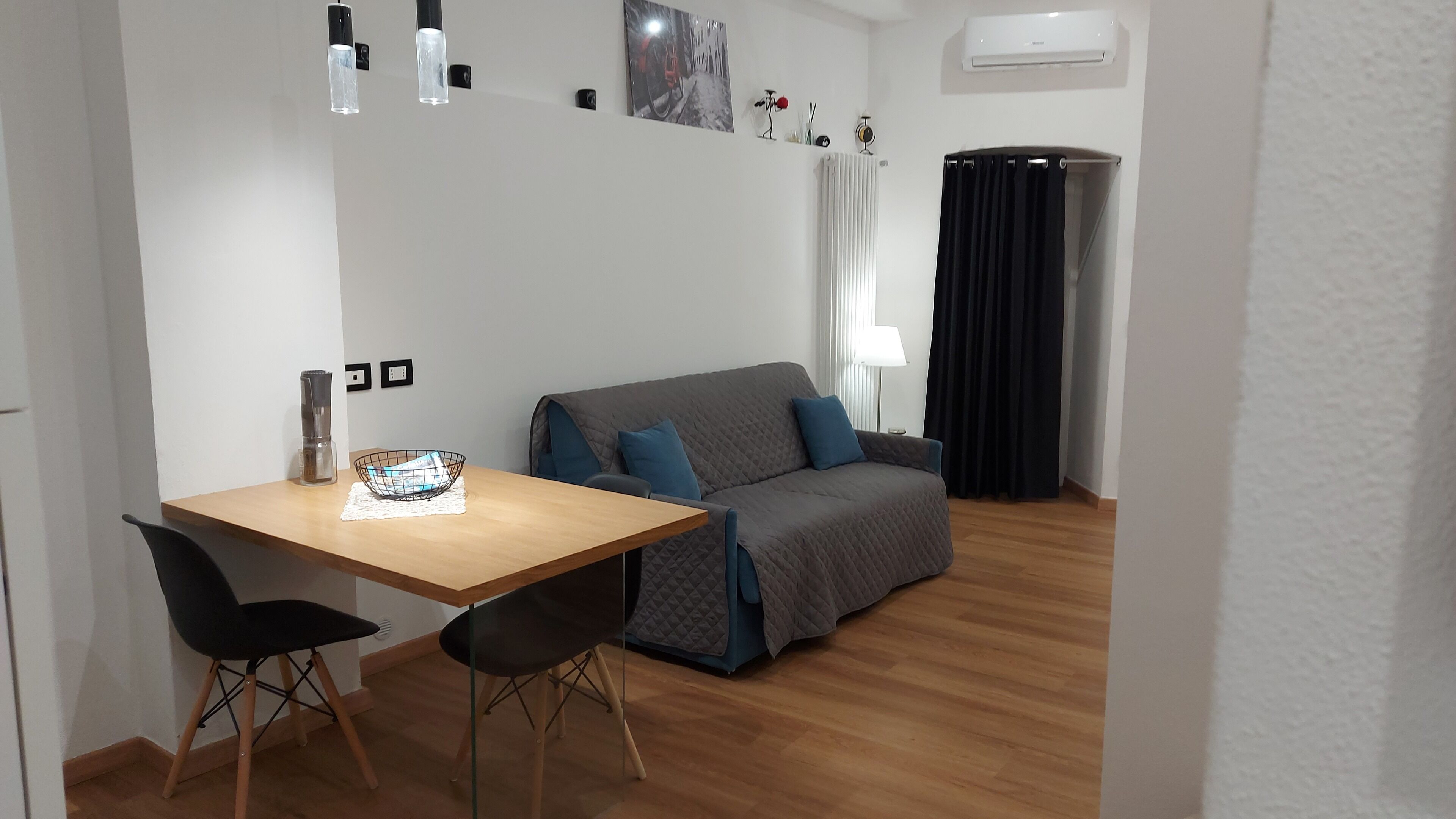 A small, modern room with a wooden table, two black chairs, a grey sofa, and a black curtain.