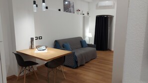 Una habitación pequeña y moderna con una mesa de madera, dos sillas negras, un sofá gris y una cortina negra.