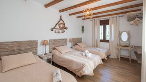 Een kamer met twee bedden, houten balken, een hanglamp, een spiegel en een raam met gordijnen.