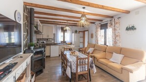 Een gezellige woonkamer met een bank en een eettafel gedekt voor vier personen. Achtergrond toont een keuken met moderne apparatuur en een groot raam.