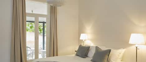 A bedroom with a bed, two bedside lamps, a window with curtains, and a hanging light fixture.