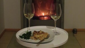 A room with a wood-burning stove, two glasses of white wine, and a plate of food on a small table.