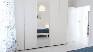Ett sovrum med en säng, en garderob, en hängande lampa och en dörr som leder till ett annat rum.