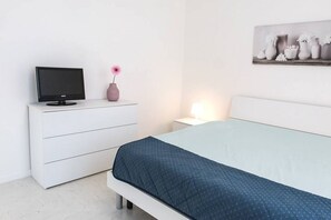 A bedroom with a bed, a TV on a dresser, a vase with a flower, and a wall-mounted picture. - C004 - Camerano, new two-room apartment with air conditioning (Camerano)