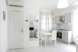 A modern kitchen with white cabinetry, a dining table with chairs, and a white door. - C004 - Camerano, new two-room apartment with air conditioning (Camerano)