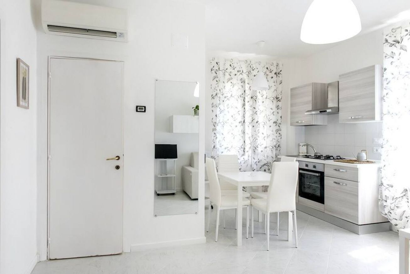 Une cuisine moderne avec des meubles blancs, une table à manger avec des chaises et une porte blanche.